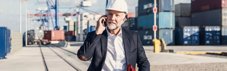 Telefonierender Mann im Hafen mit Anzug und Helm